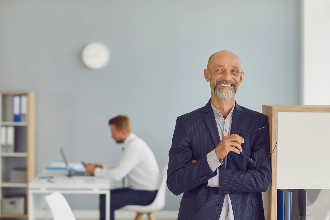 Smiling senior executive in a navy pinstripe suit standing in a bright office